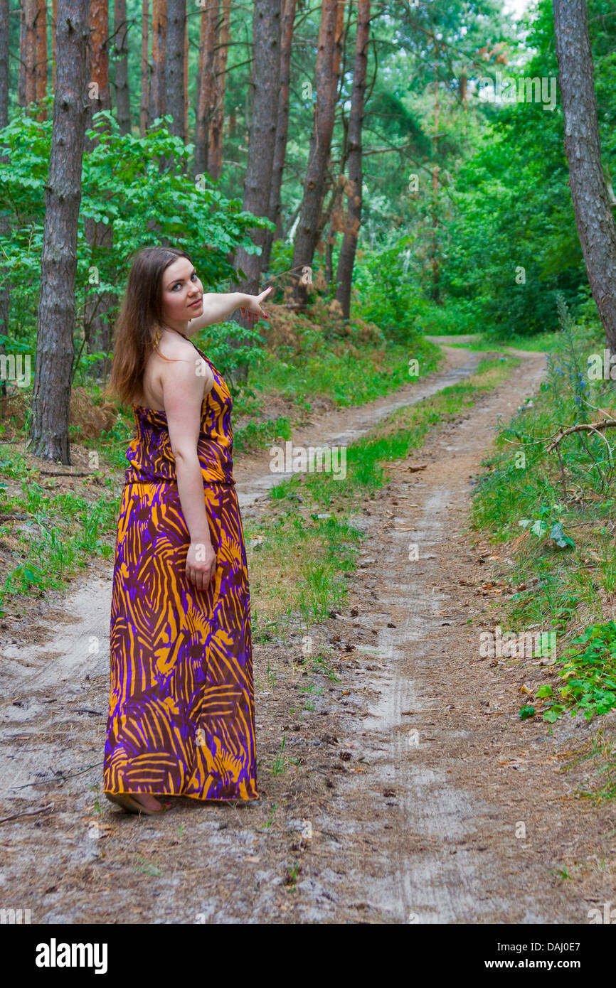 Pretty young woman standing on the forest road with a hand pointing forward Stock Photo