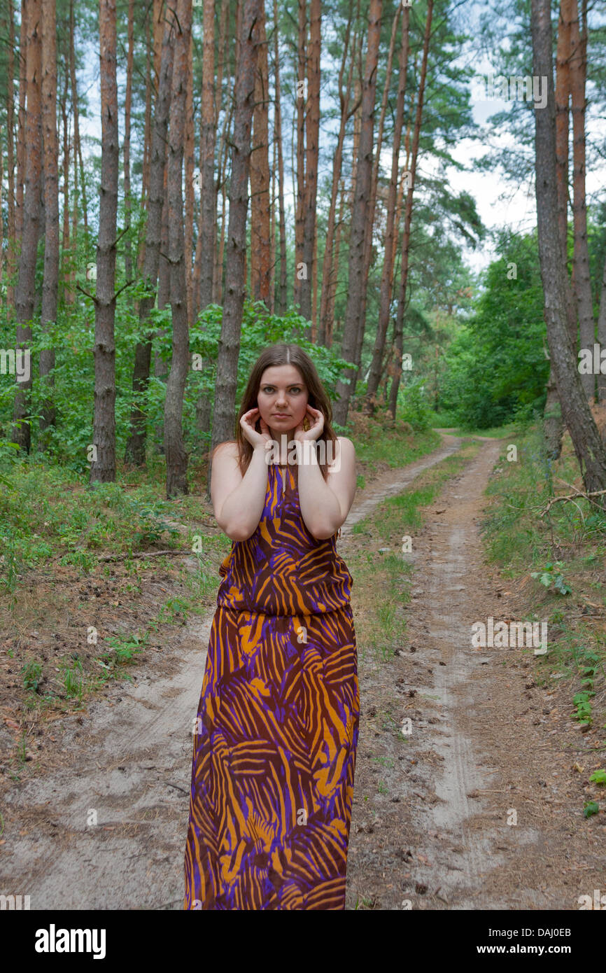 Pretty young woman standing on the forest road with raised hands Stock Photo