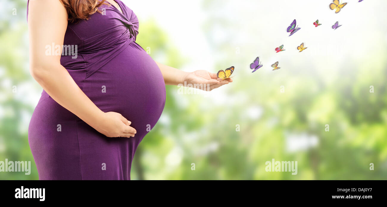 Pregnant woman holding her belly and butterflies on her hand in a park Stock Photo
