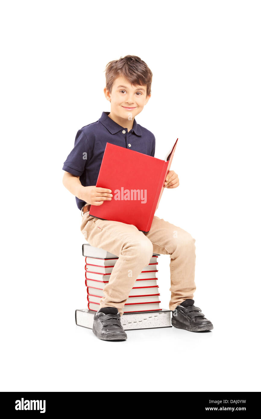 Smiling school boy sitting on a pile of books and reading Stock Photo ...