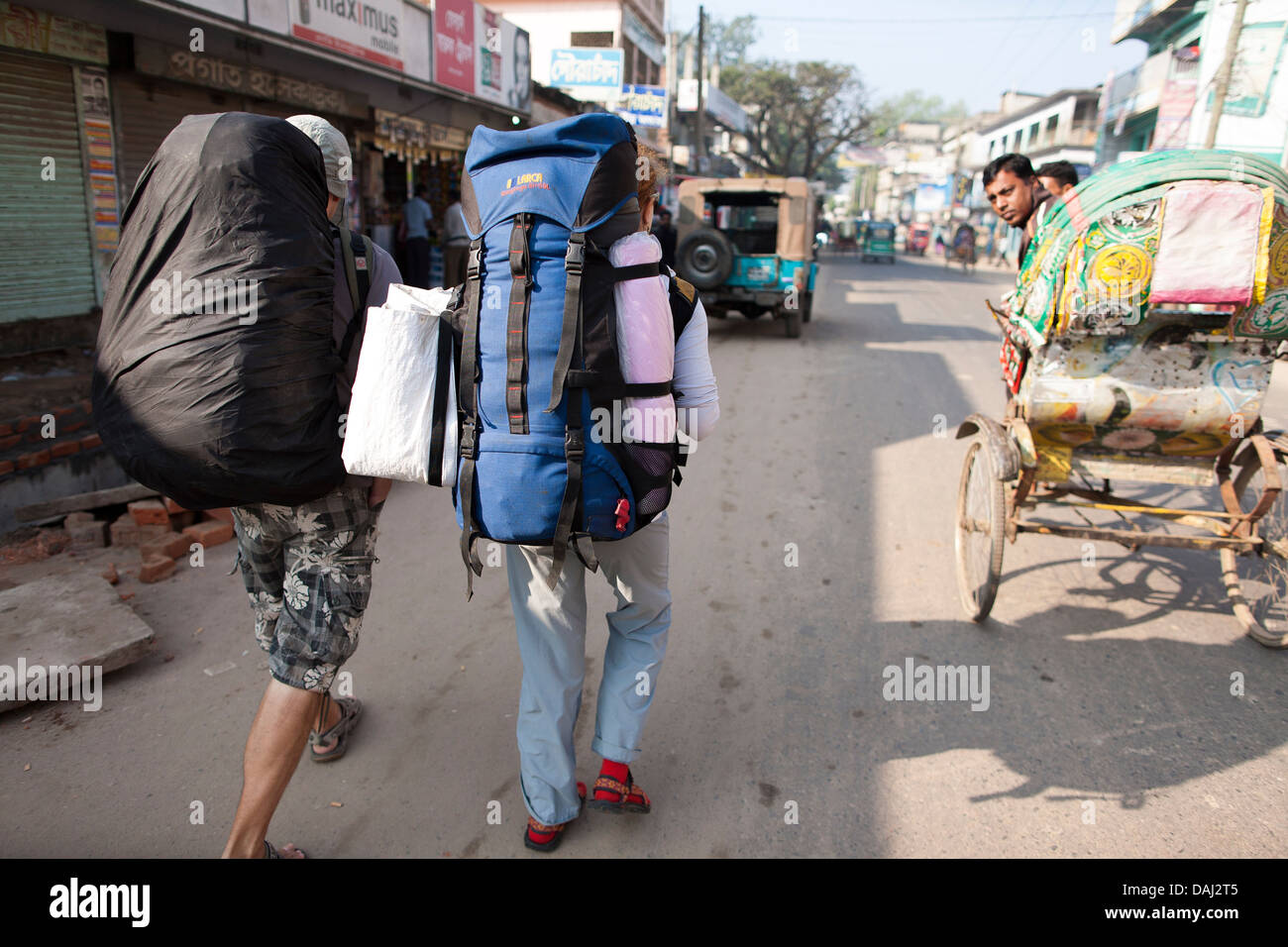 Backpackers, traveling through Bangladesh and South east Asia walkalong the streets of Srimongol to catch a bus carrying packs. Stock Photo