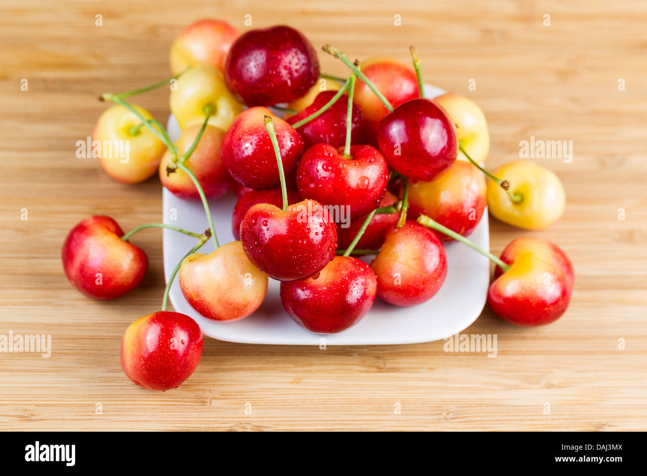 Horizontal photo of Rainier cherries, with water drops, in white dish on natural bamboo board Stock Photo