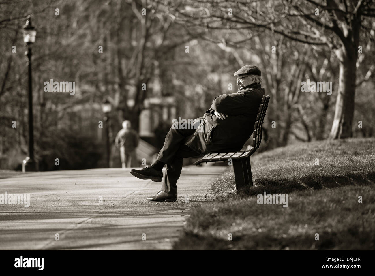 A senior man wearing a cap sitting on a park bench on Primrose Hill, London Stock Photo
