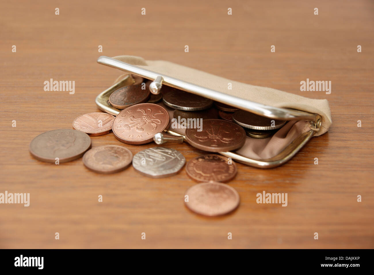 A purse filled with coins (British sterling money) spilling out onto a table Stock Photo