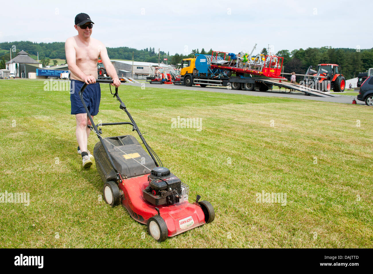 Builth Wells, Mid Wales, UK. 15th July 2013. A workman cuts the grass for a marquee plot. Workmen preparing The Royal Wesh Showground for the start of biggest Agricultural show in Britain next Monday 22nd July 2013 find the heat heavy going as temperatures remain above 30 degrees celsius. Photo credit: Graham M. Lawrence/Alamy Live News. Stock Photo