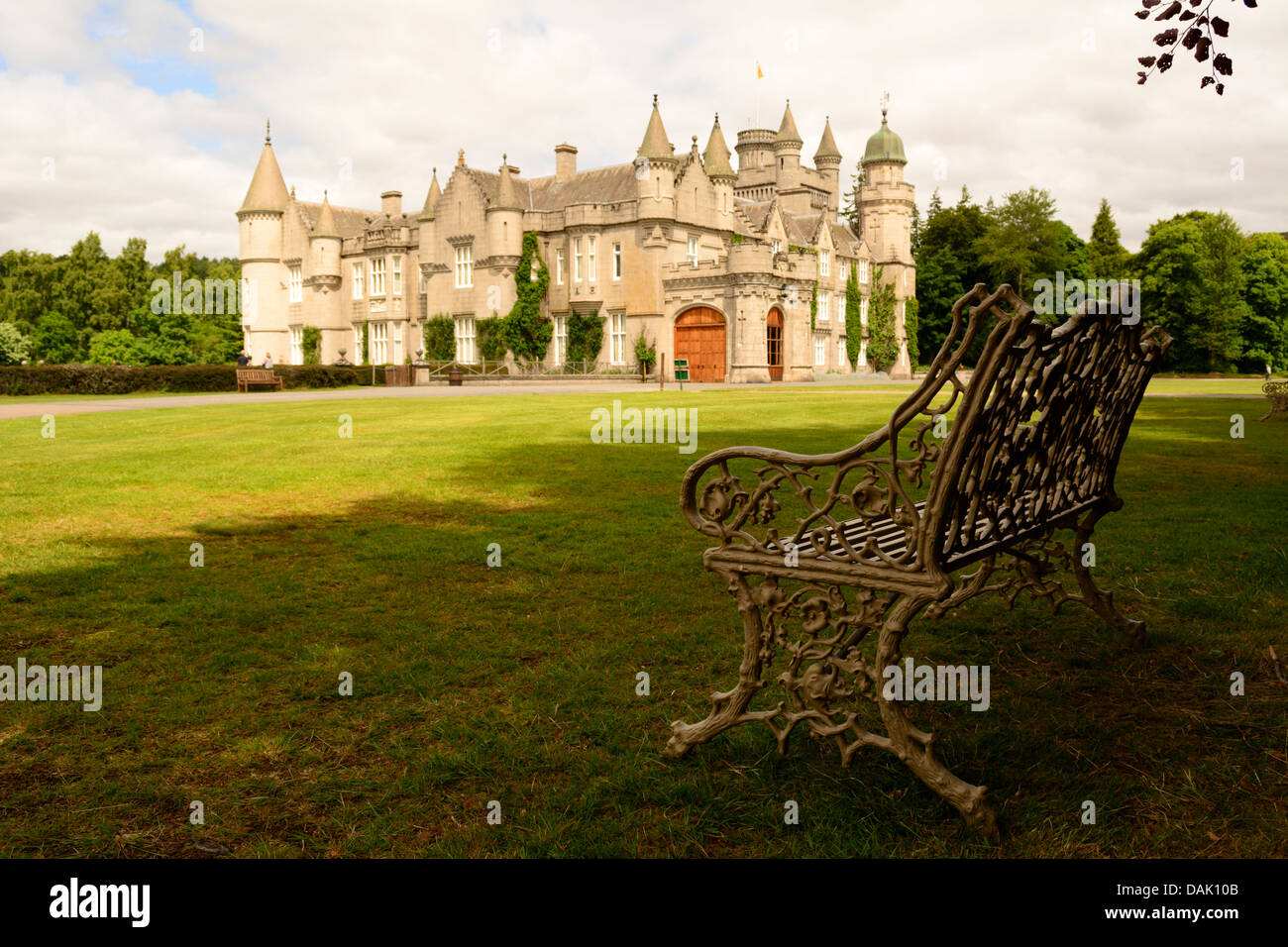 Horizontal view of Balmoral Castle, the Royal Family's summer residence, from garden on a sunny day with bench in foreground Stock Photo