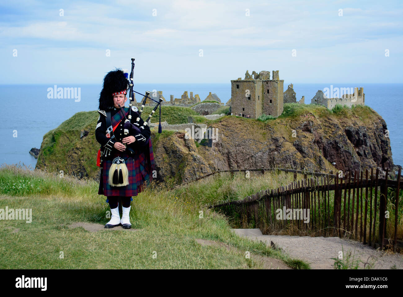 Horizontal image of a piper playing bagpipes in front of Dunnottar Castle, Scotland, UK, 8th wonder of the world nominee Stock Photo
