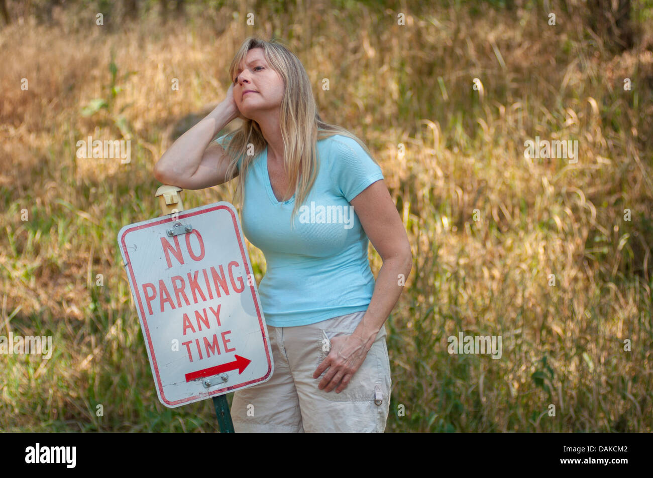Woman leaning against a No Parking Any Time zone with the arrow pointing at her. Stock Photo