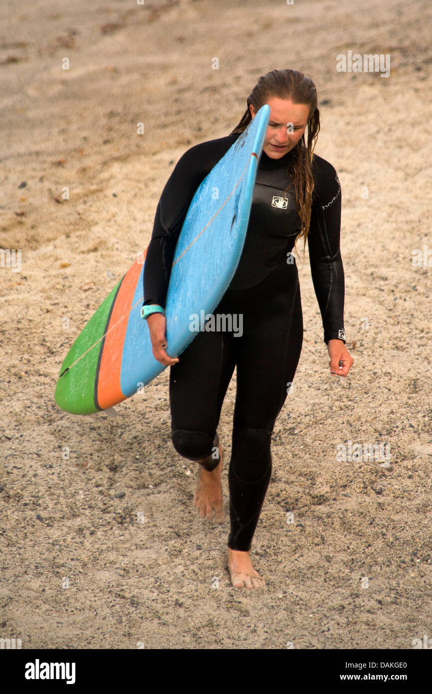 Wearing wetsuit and carrying surfboard, teenage boy member of the high school surfing team