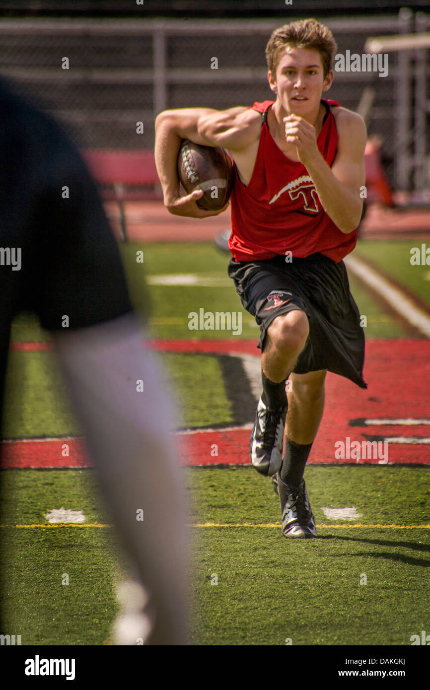A muscular and determined high school athlete runs with the ball during spring football practice in San Clemente, CA. Stock Photo