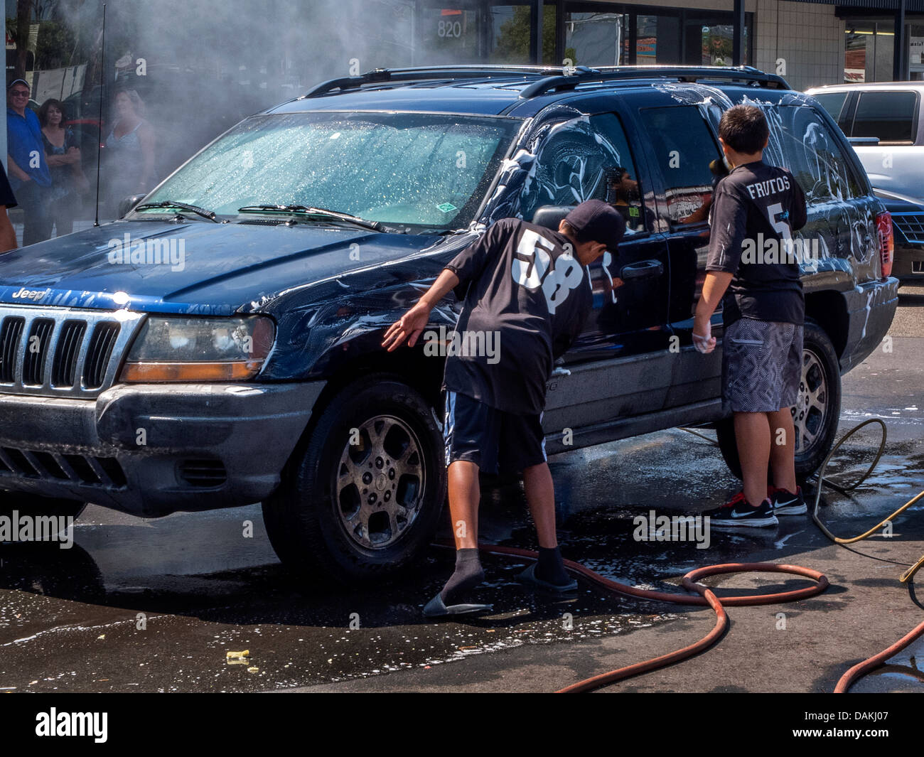 Multiethnic local children assist at a fund-raising charity car wash in a Southern California strip mall on a sunny afternoon. Stock Photo
