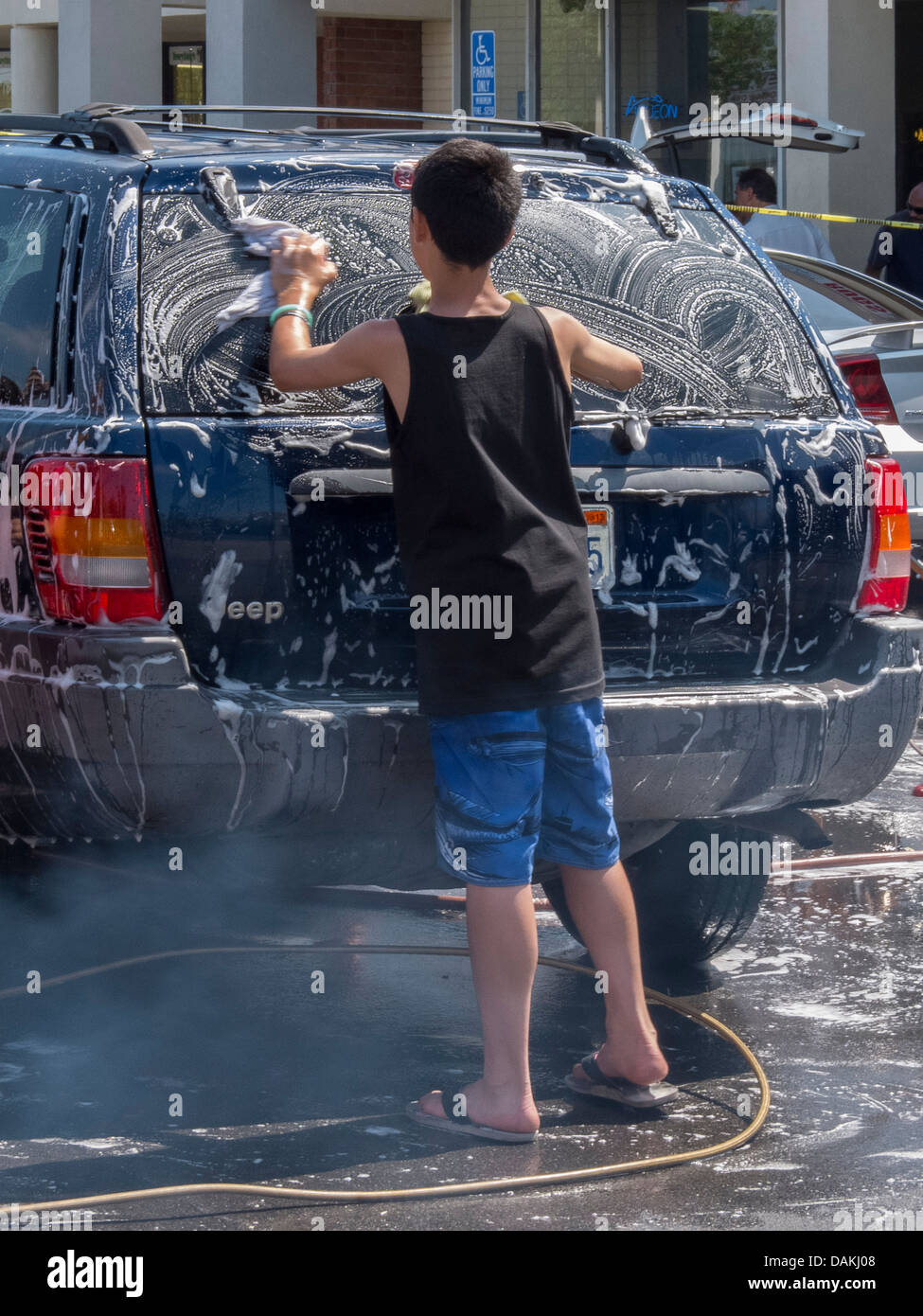 A local boy assists at a fund-raising charity car wash in a Southern California strip mall on a sunny afternoon. Stock Photo