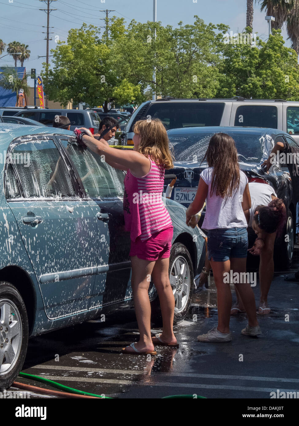 Multiethnic local children assist at a fund-raising charity car wash in a Southern California strip mall on a sunny afternoon. Stock Photo