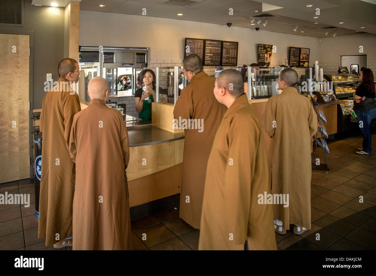 Contrasting with their surroundings, three Buddhist monks and one nun in brown robes and shaved heads, buy drinks in Starbucks. Stock Photo