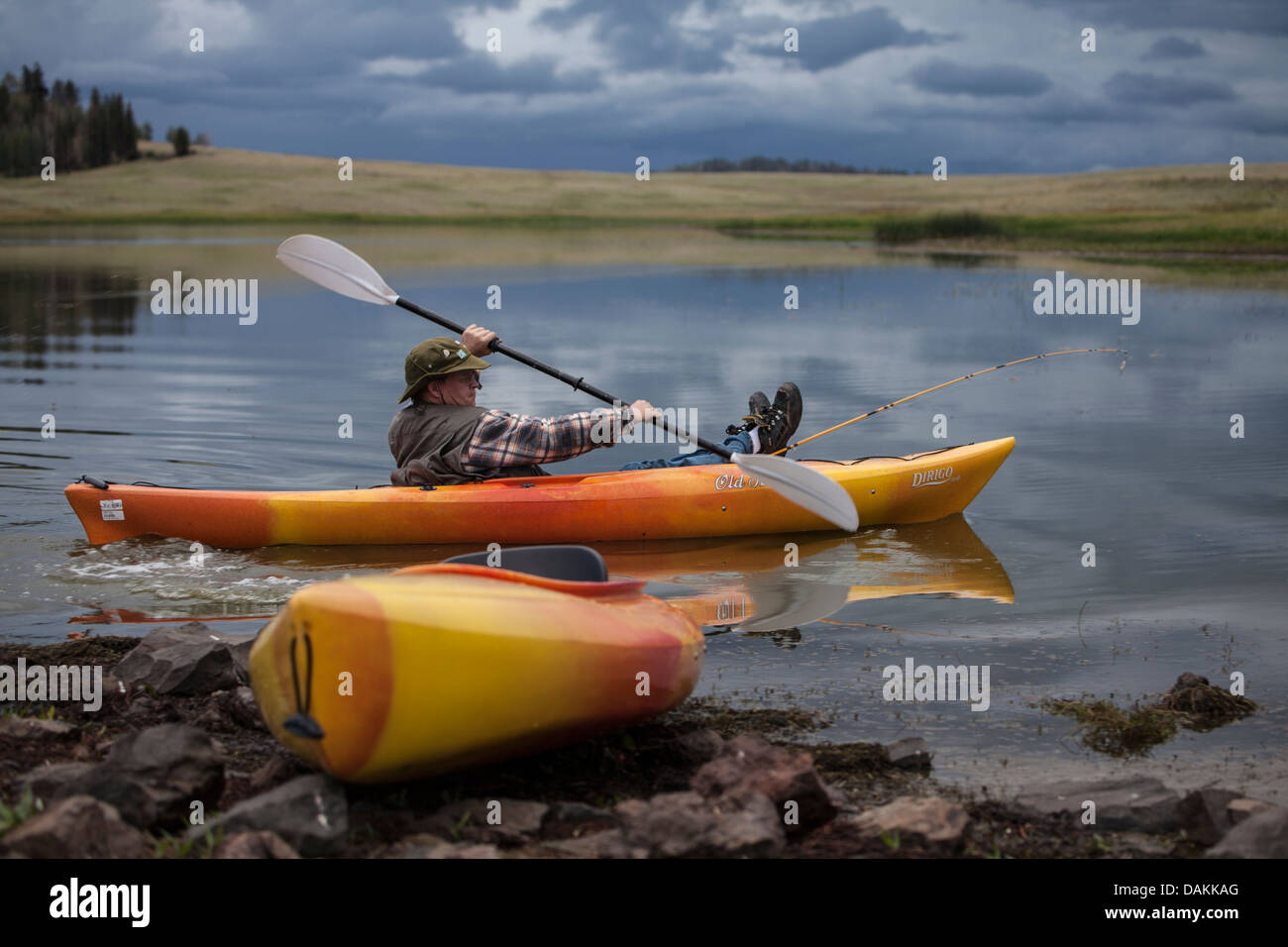 Young man in yellow orange kayak is paddling into a lake in Arizona with his feet and fishing pole propped up on front of boat. Stock Photo