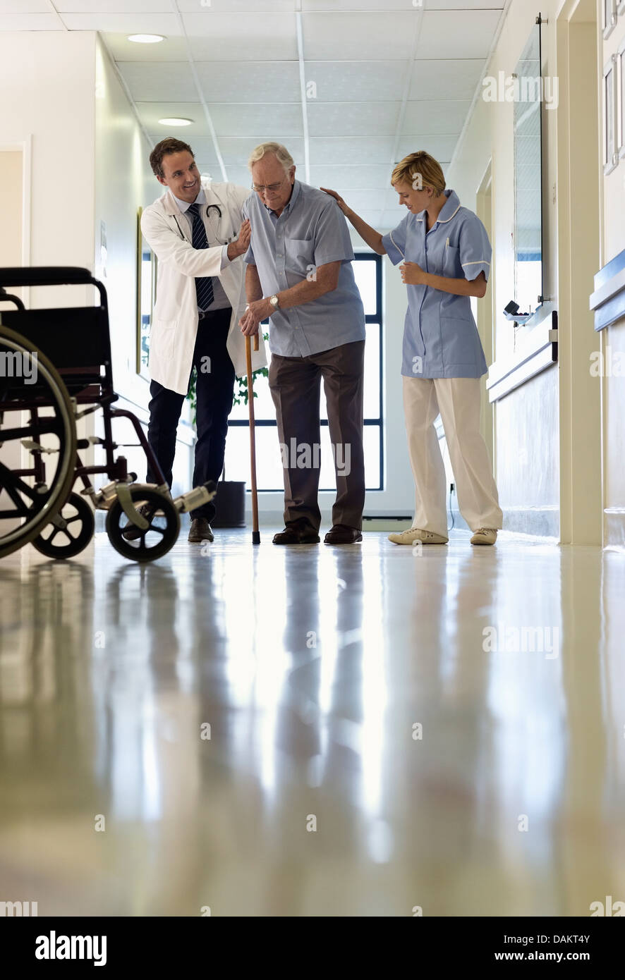 Doctor and nurse helping older patient walk in hospital Stock Photo