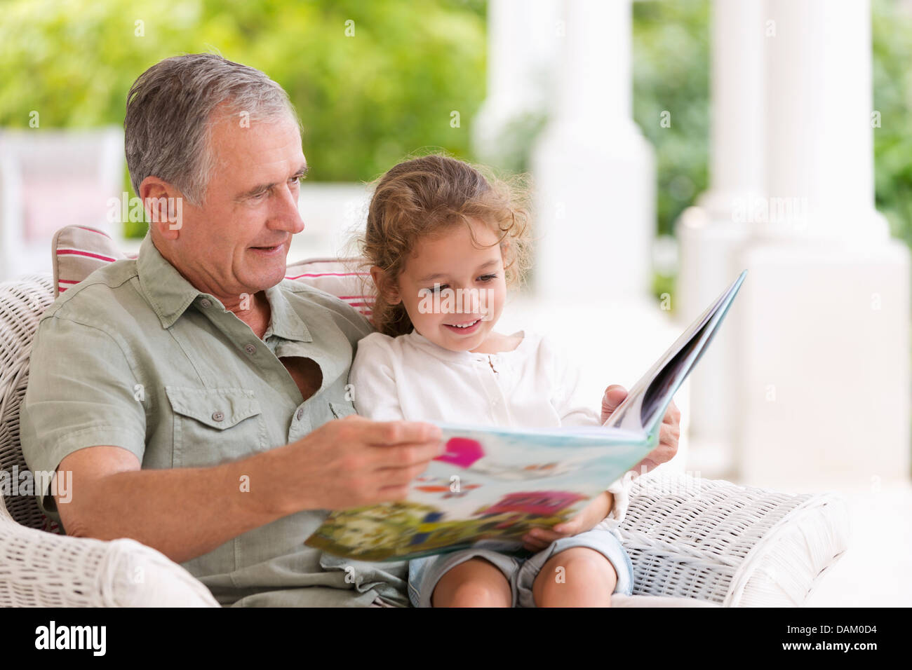 Older man reading to granddaughter on porch Stock Photo