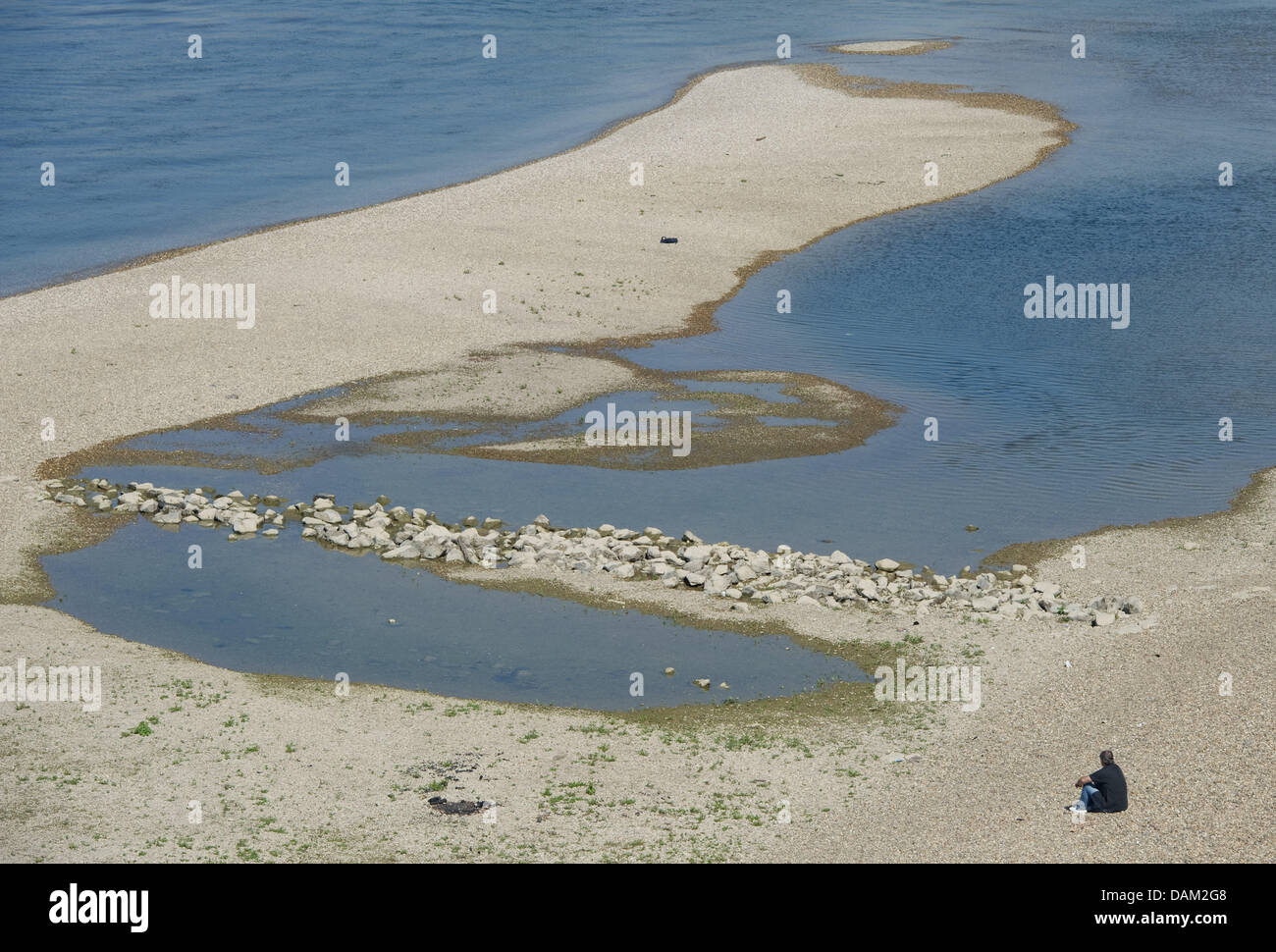 A man sits near a sand bank that has emerged due to a low water level of the Rhine river in Speyer, Germany, 18 May 2011. The recent drought in the south of Germany causes low water levels. Photo: Uwe Anspach Stock Photo