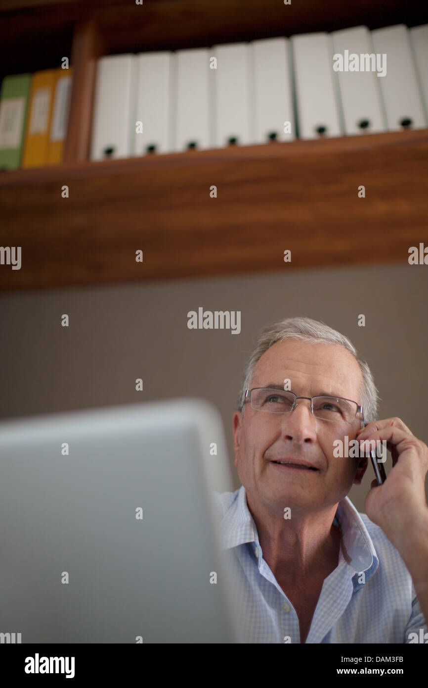 Older man talking on cell phone at desk Stock Photo
