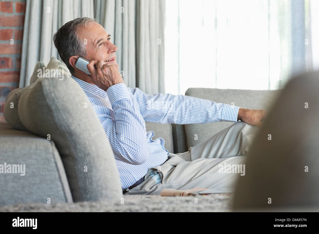 Older man talking on cell phone on sofa Stock Photo