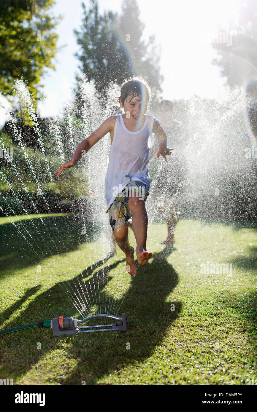 Boy playing in sprinkler in backyard Stock Photo