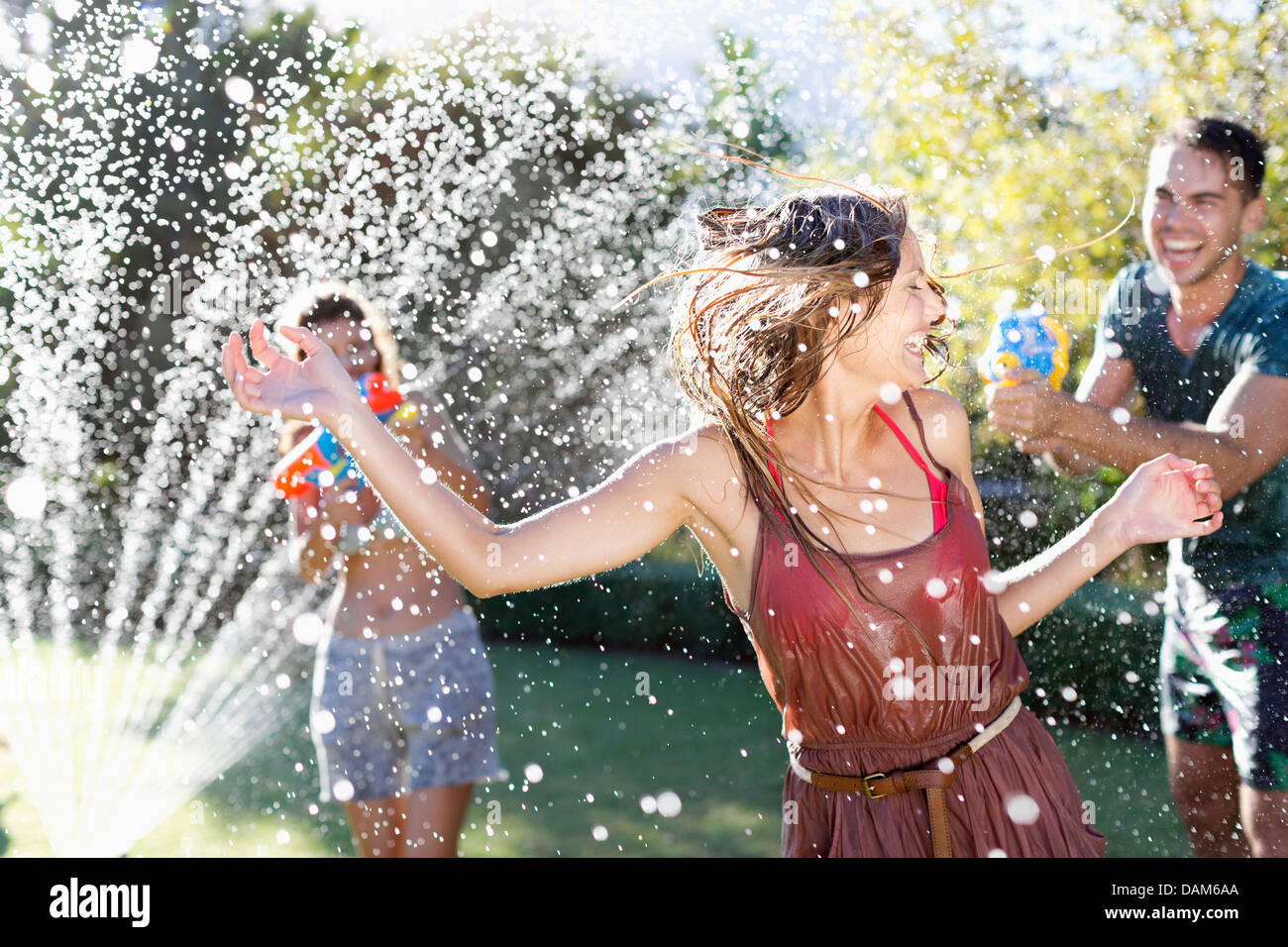 Friends playing with water guns in sprinkler Stock Photo