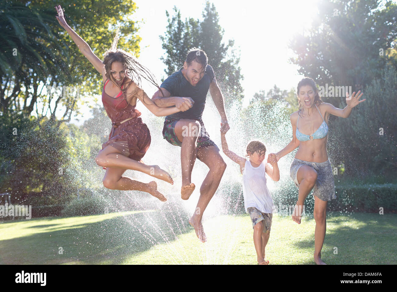 Family jumping in sprinkler Stock Photo