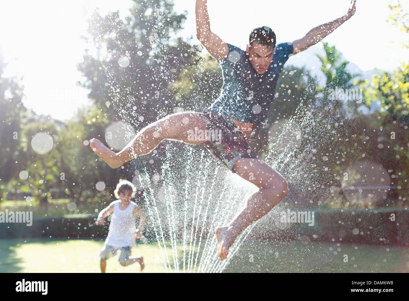 Father and son playing in sprinkler in backyard Stock Photo