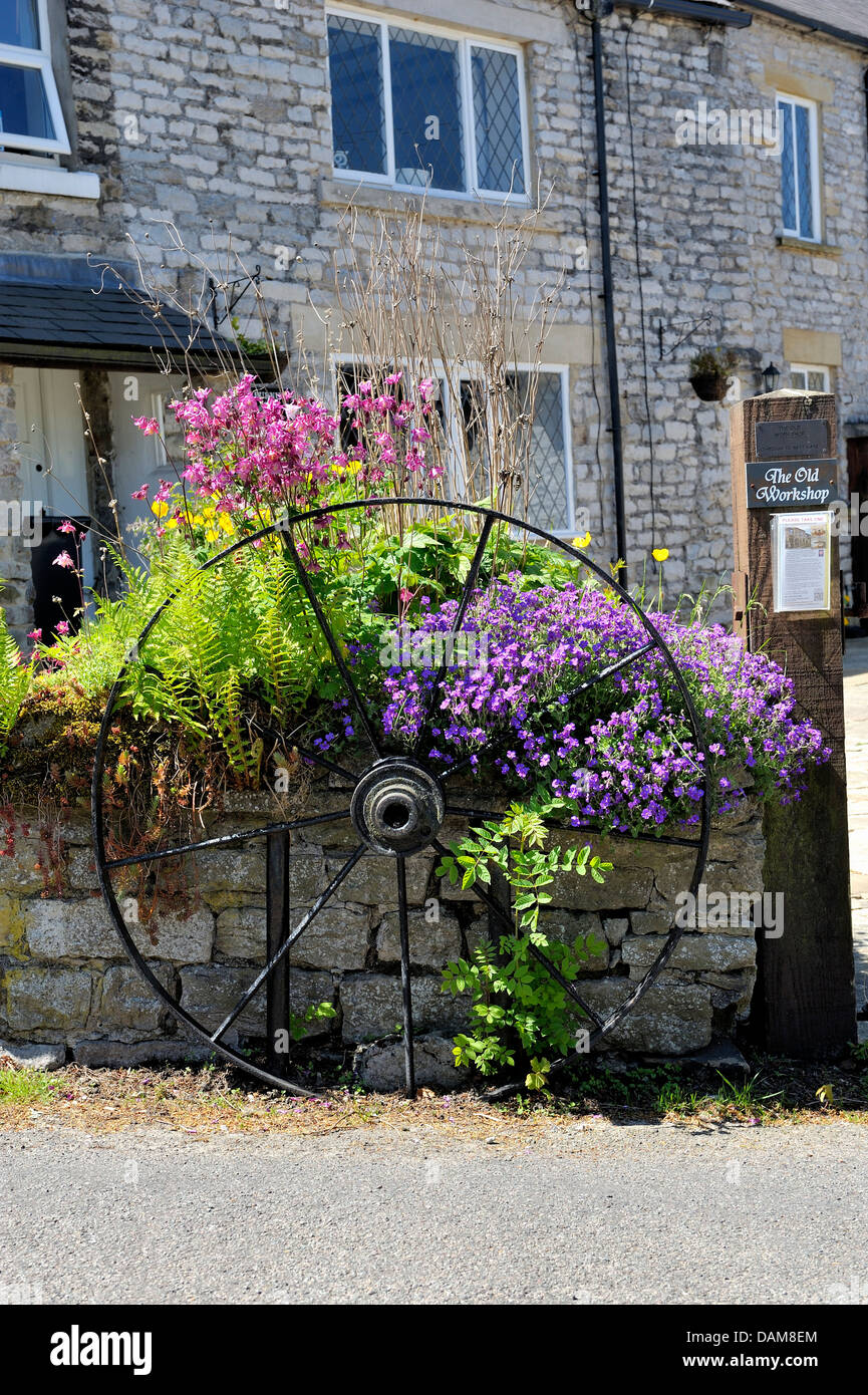old wagon wheel on a stone wall surrounded by flowers Castleton Derbyshire England uk Stock Photo
