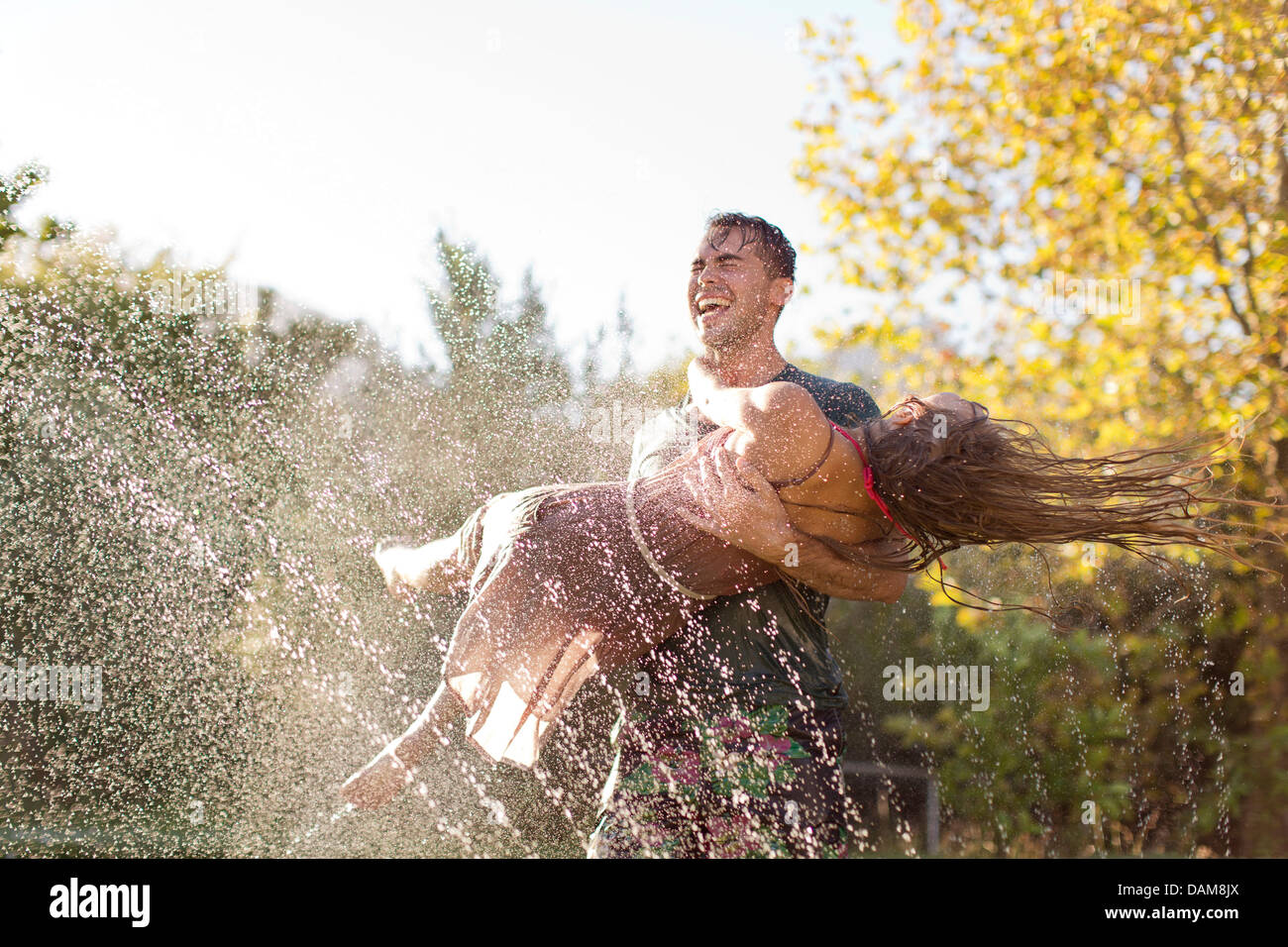Couple playing in sprinkler in backyard Stock Photo