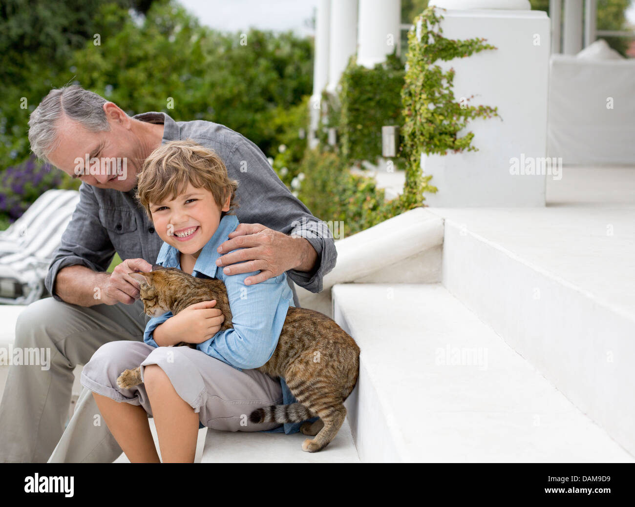 Older man and grandson petting cat on steps Stock Photo