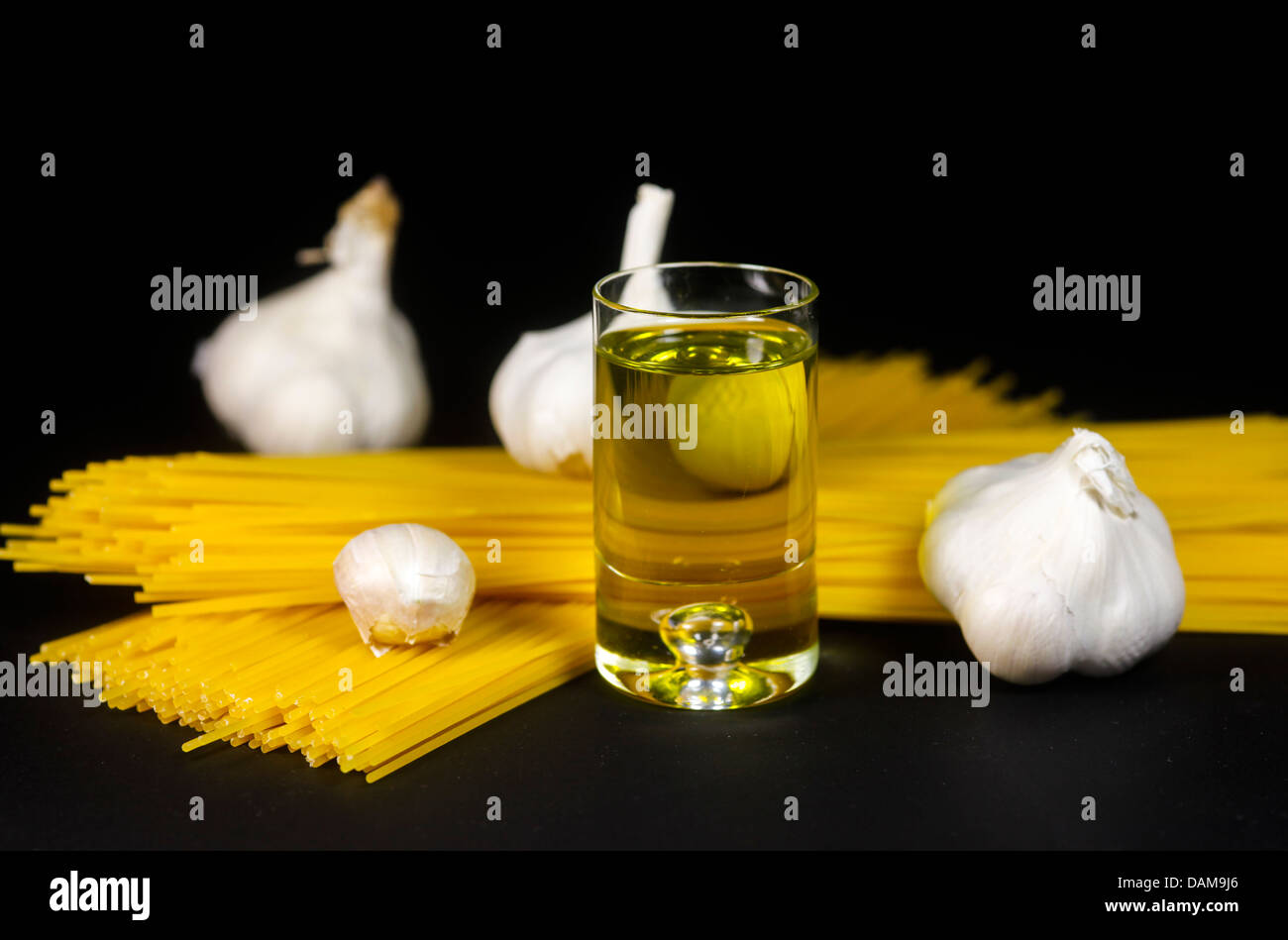 Glass of olive oil with spaghetti and garlics on black bakground, close up Stock Photo