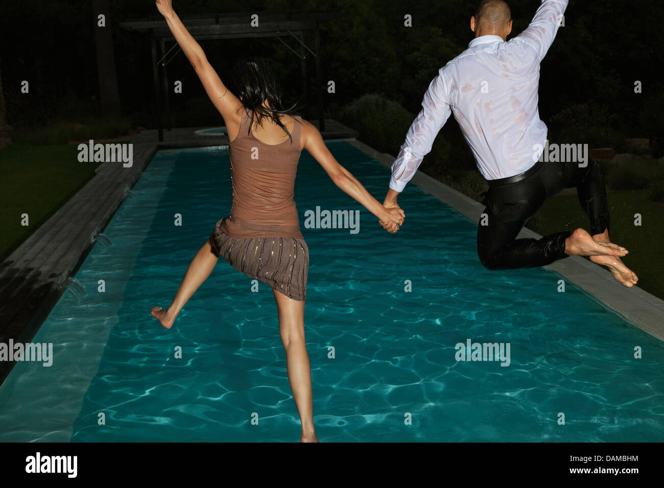 Fully dressed friends jumping into swimming pool Stock Photo