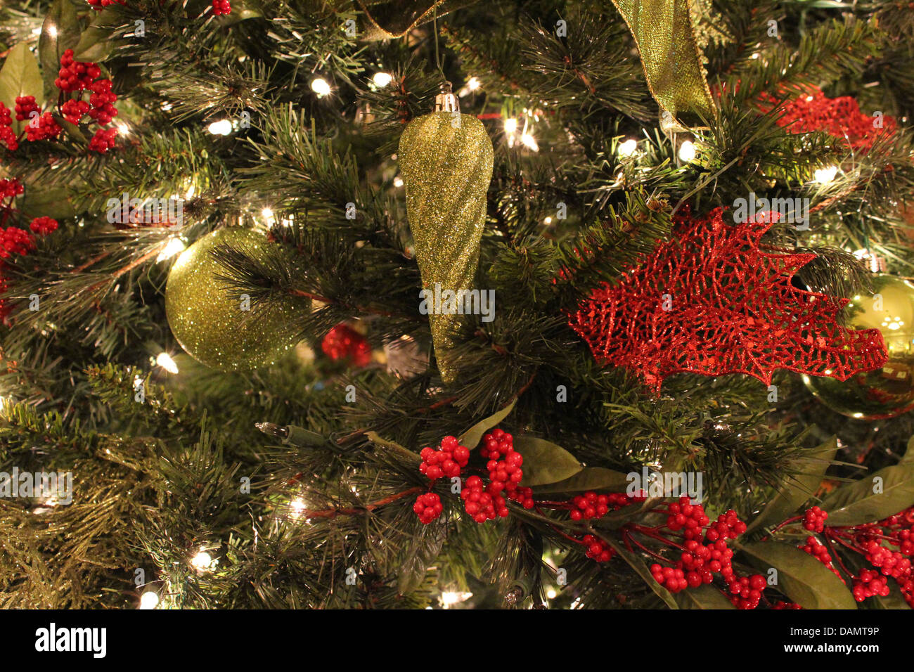 Colorful red and gold embellishments on green pine tree branches with little twinkling lights wound throughout. Stock Photo