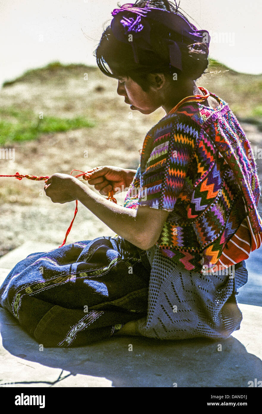 Young Caqchiquel Mayan girl in traditional dress weaving a pulsera bracelet on the shores of Lake Atitlan, Guatemala. Stock Photo