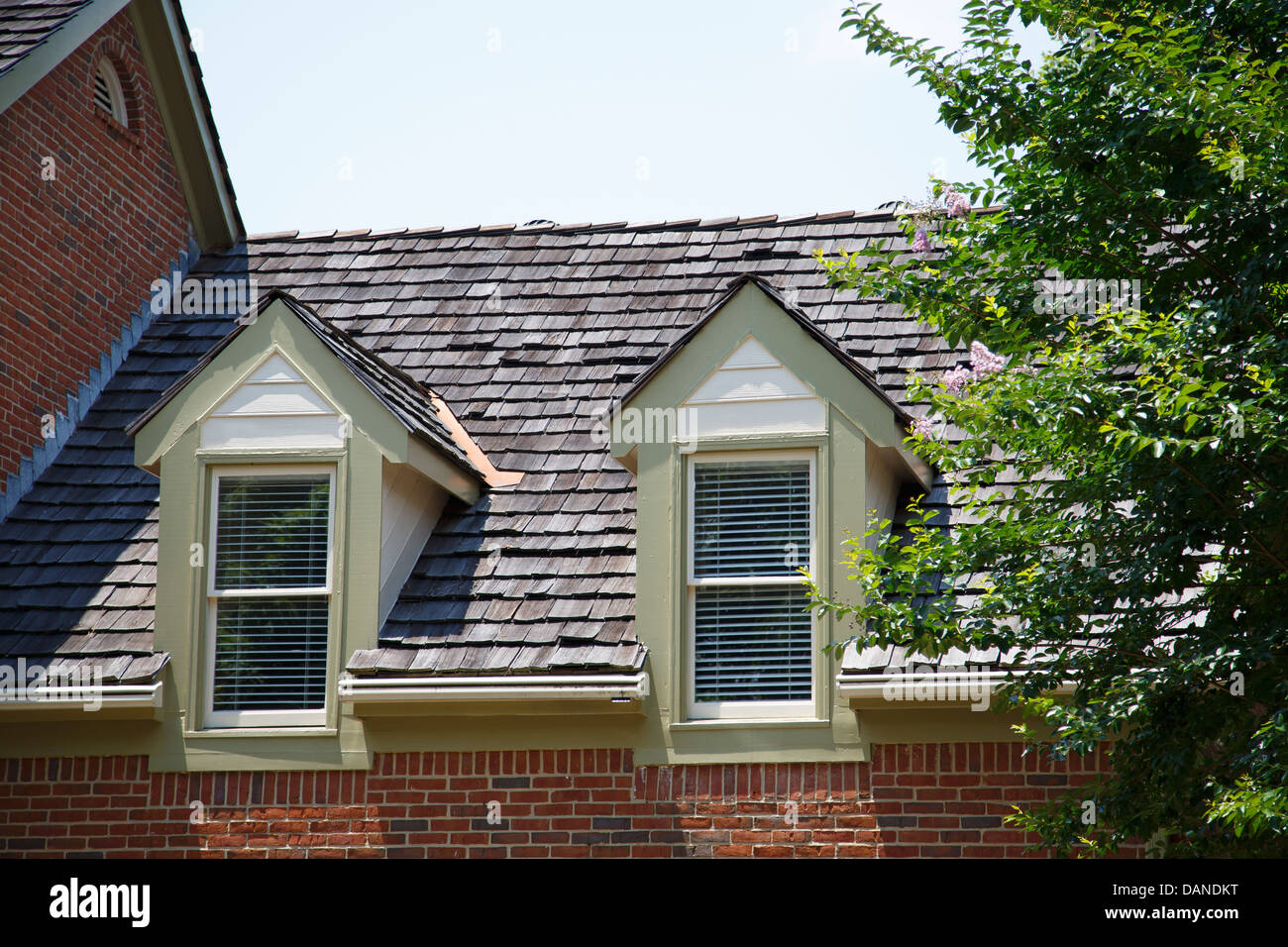 Two dormers in roof with wood shingles on a brick townhouse Stock Photo