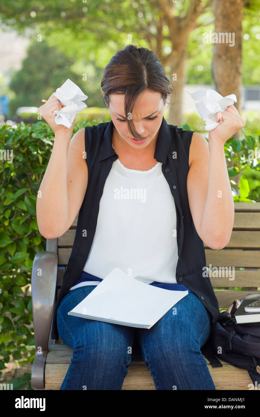 Frustrated and Upset Young Woman with Pencil and Crumpled Paper in Her Hands Sitting on Bench Outside. Stock Photo