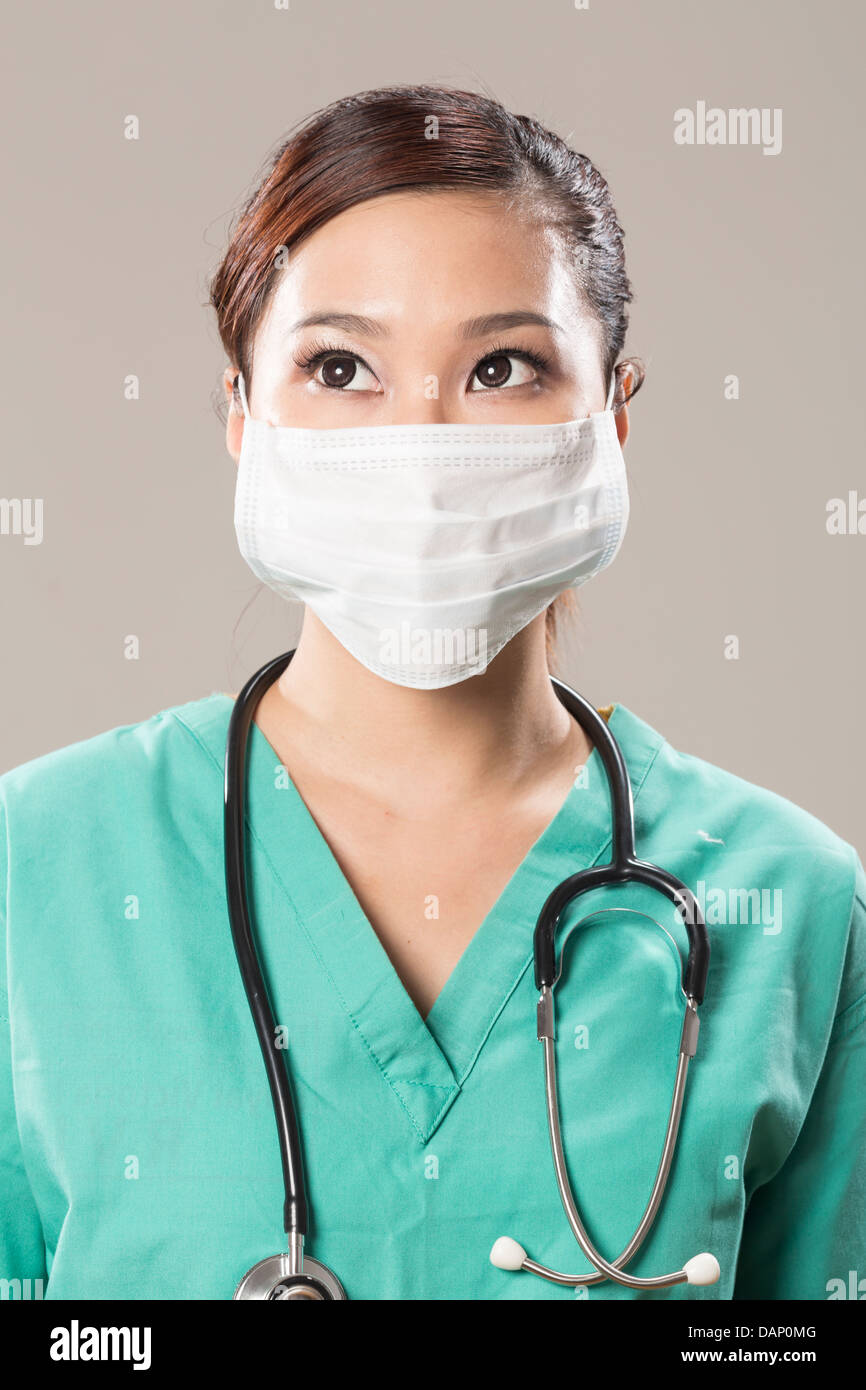 Chinese doctor wearing a face mask, green scrubs and stethoscope. Looking upwards. Stock Photo