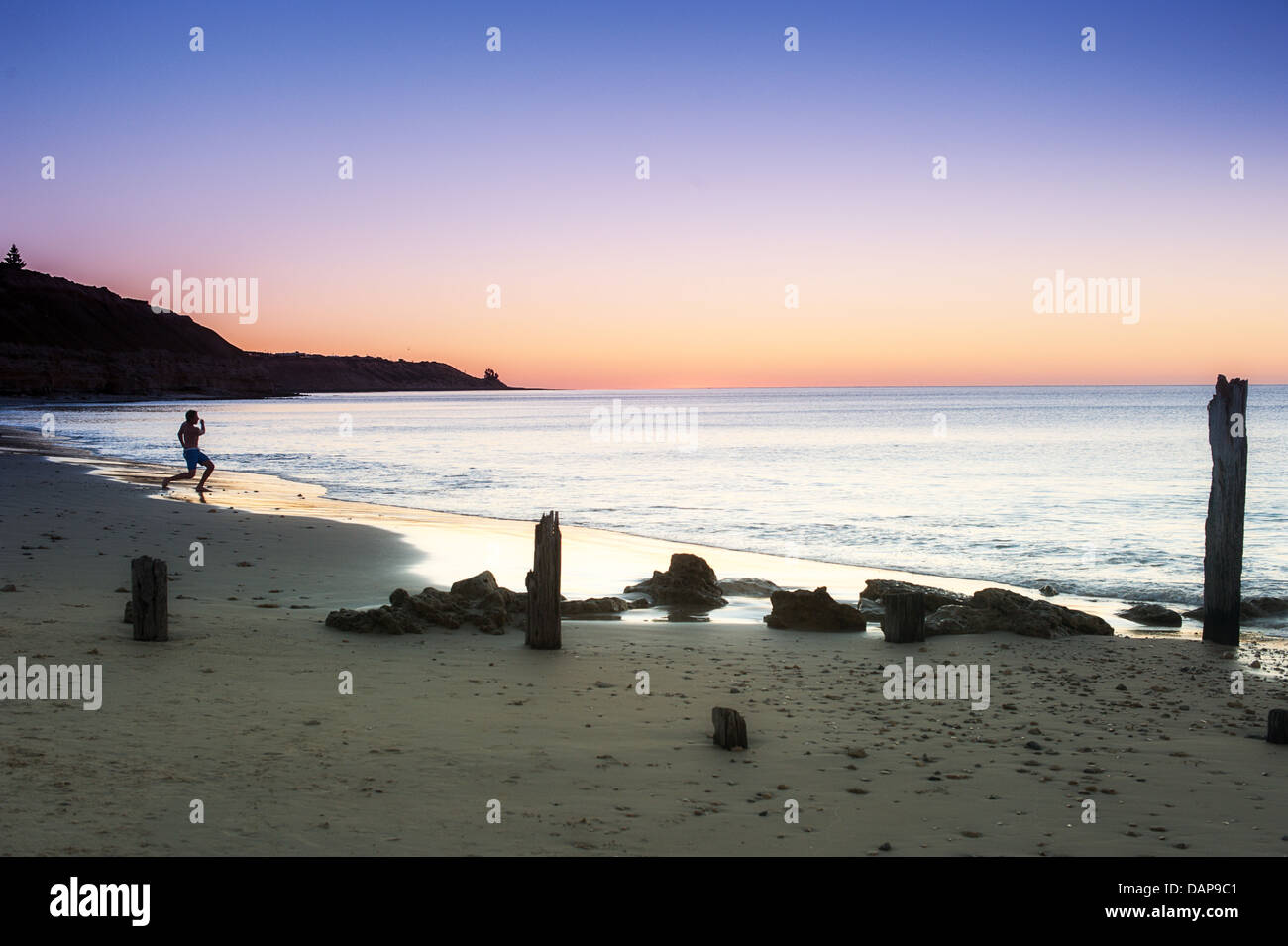 A silhouette of a person skipping stones at sunset on the calm waters of Australia's Port Willunga beach. Stock Photo