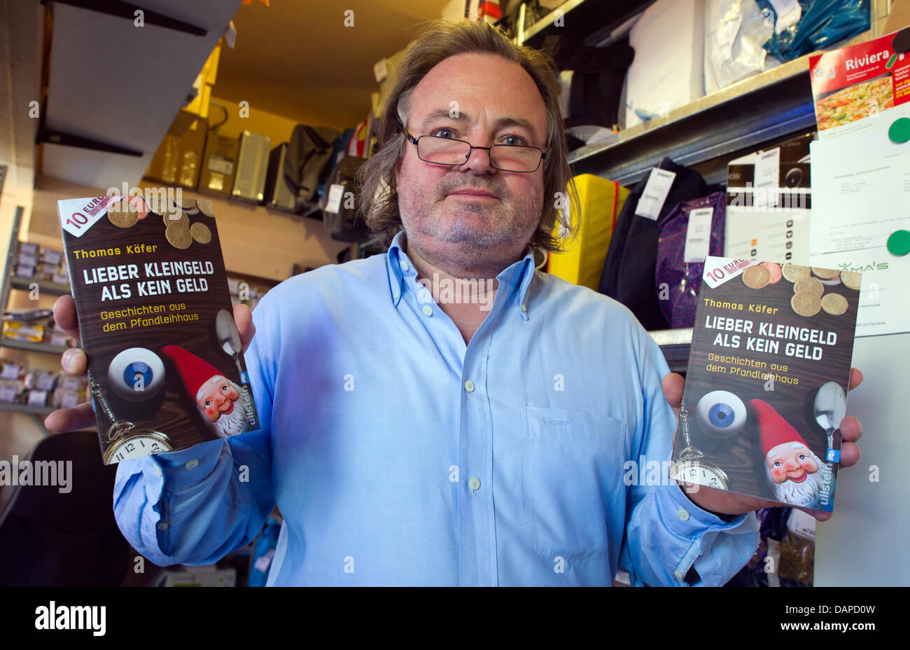 The pawnbroker Thomas Kaefer presents his book 'Lieber Kleingeld als kein Geld' ('Rather coins than no money') behind the window of the counter of his pawnbroking in Munich, Germany, 12 August 2011. Kaefer wrote about his experiences in his business. Photo: PETER KNEFFEL Stock Photo