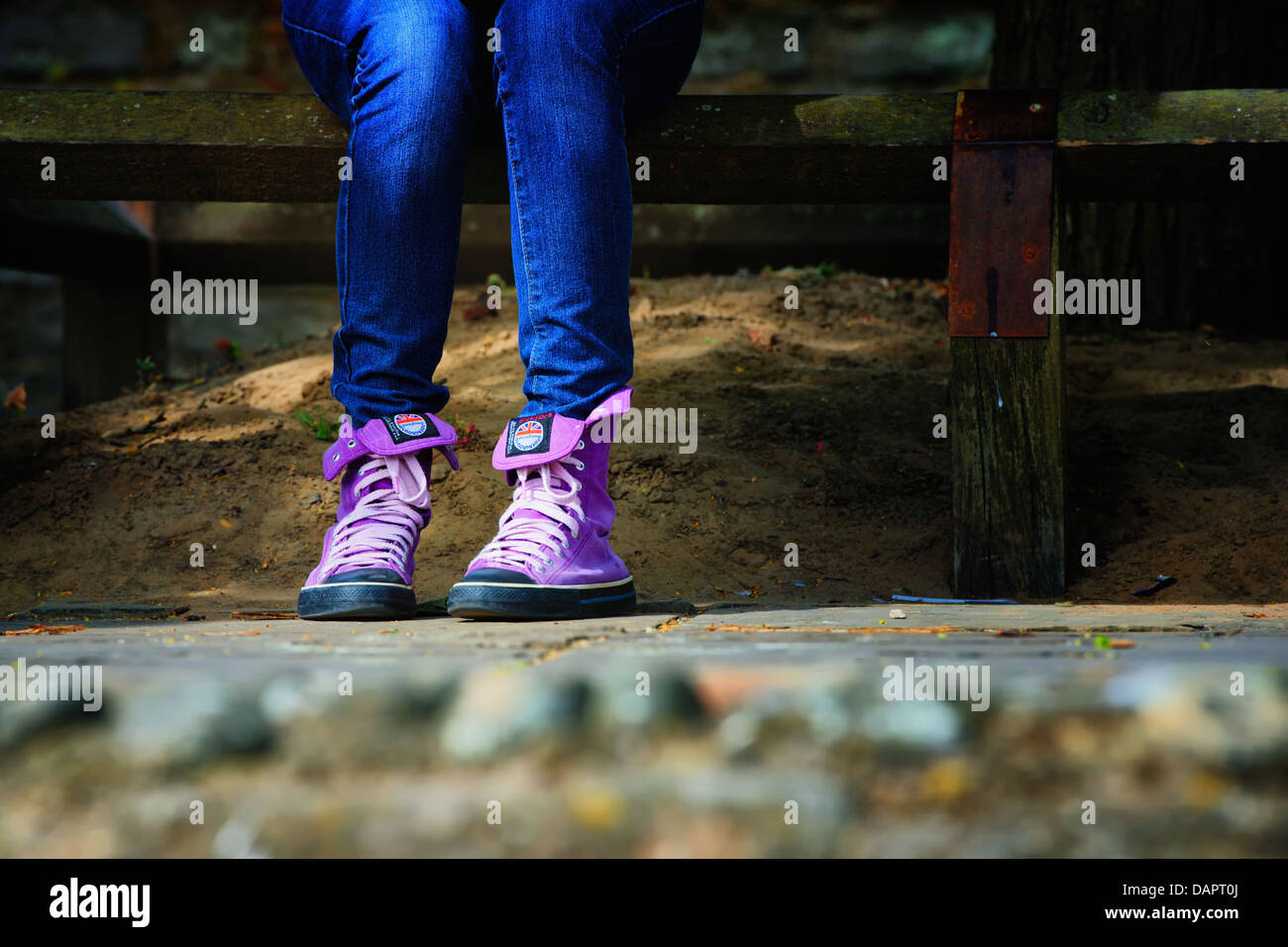 Trendy, hot pink high top sneakers worn with tight jeans on a woman sat down on a  fence. Stock Photo