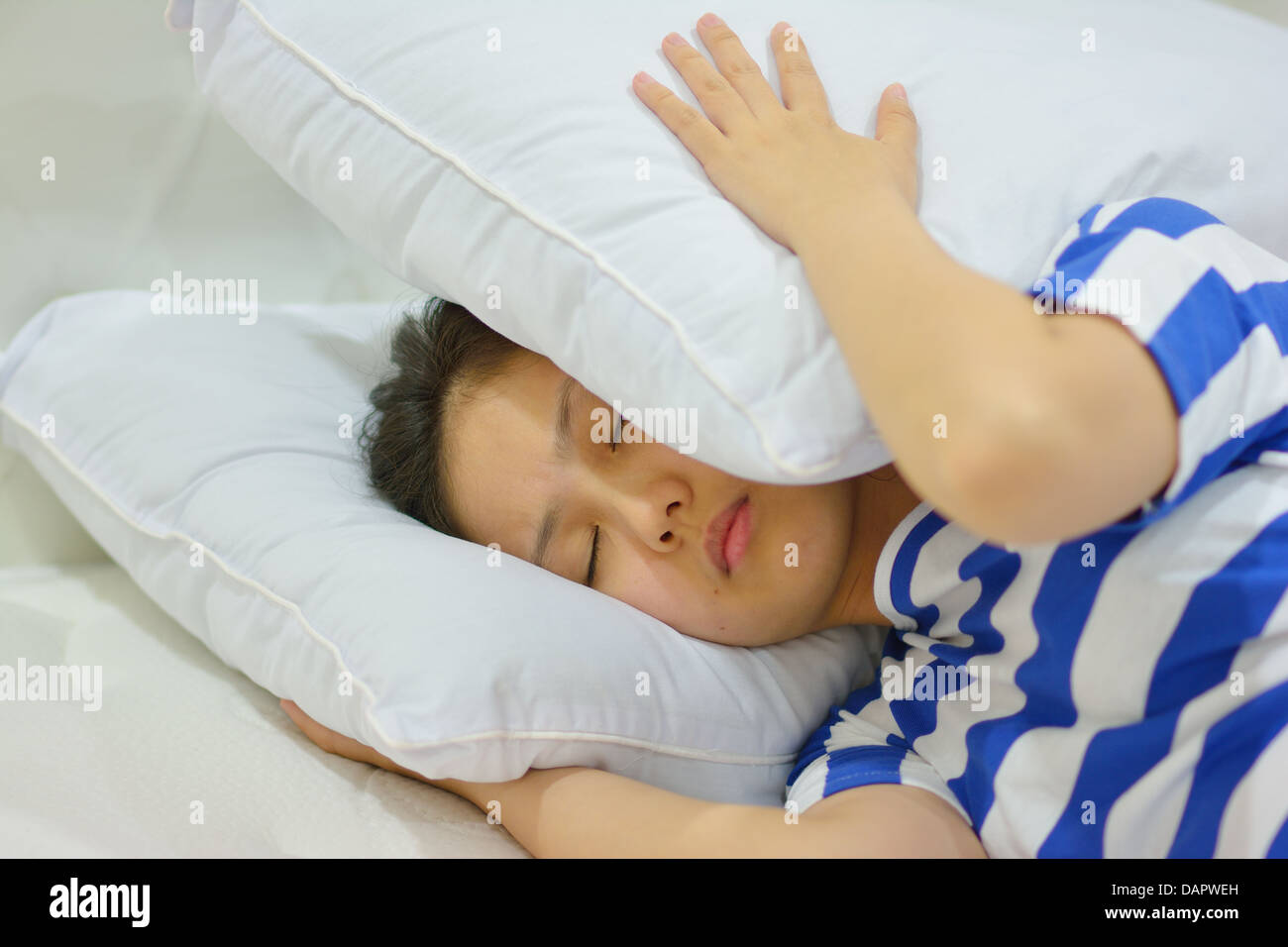 young woman suffering from insomnia and covering her head with a pillow Stock Photo