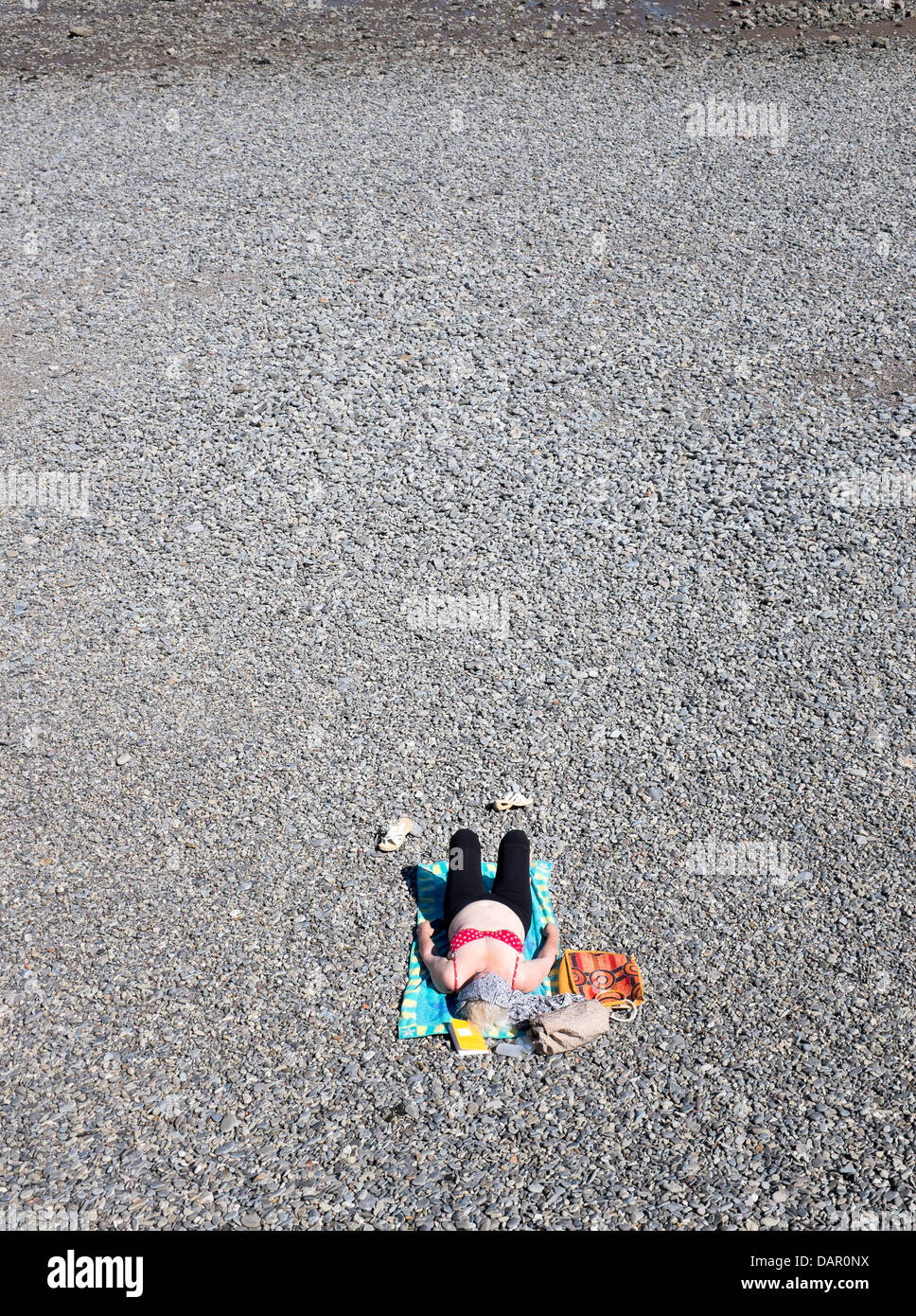 Young Woman sunbathing alone on pebbled beach at Penarth Stock Photo