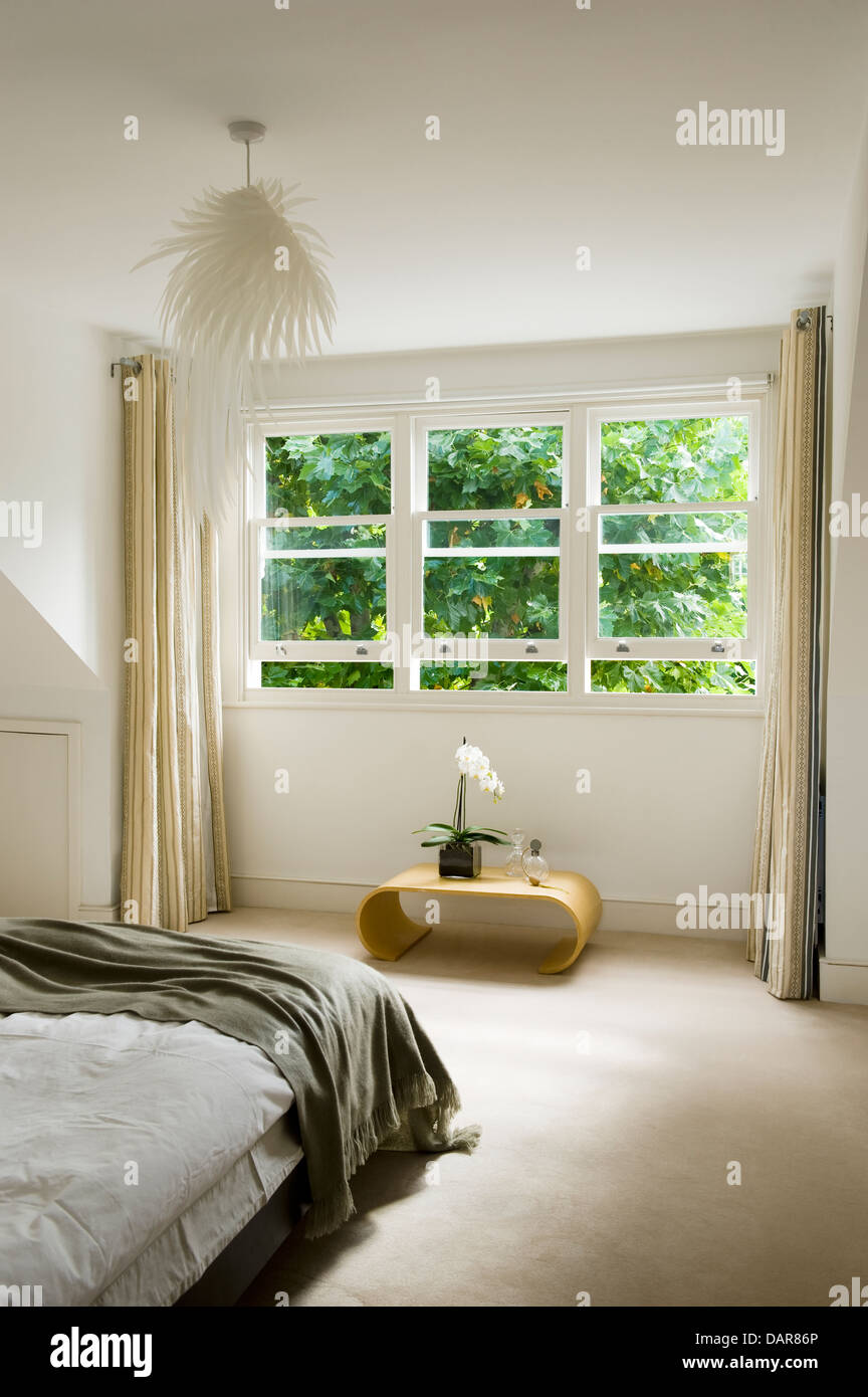 Victorian sash windows above simple side table in bedroom with feather statement light Stock Photo