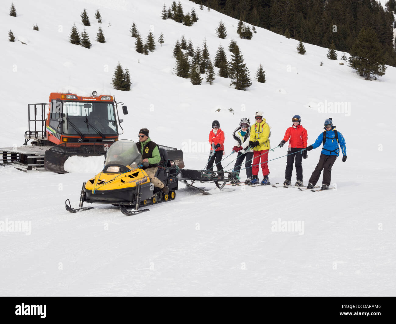 Skiers being towed by free Ski-doo snowmobile ride to Gite du Lac de Gers restaurant in Le Grand Massif ski area. Samoëns France Stock Photo