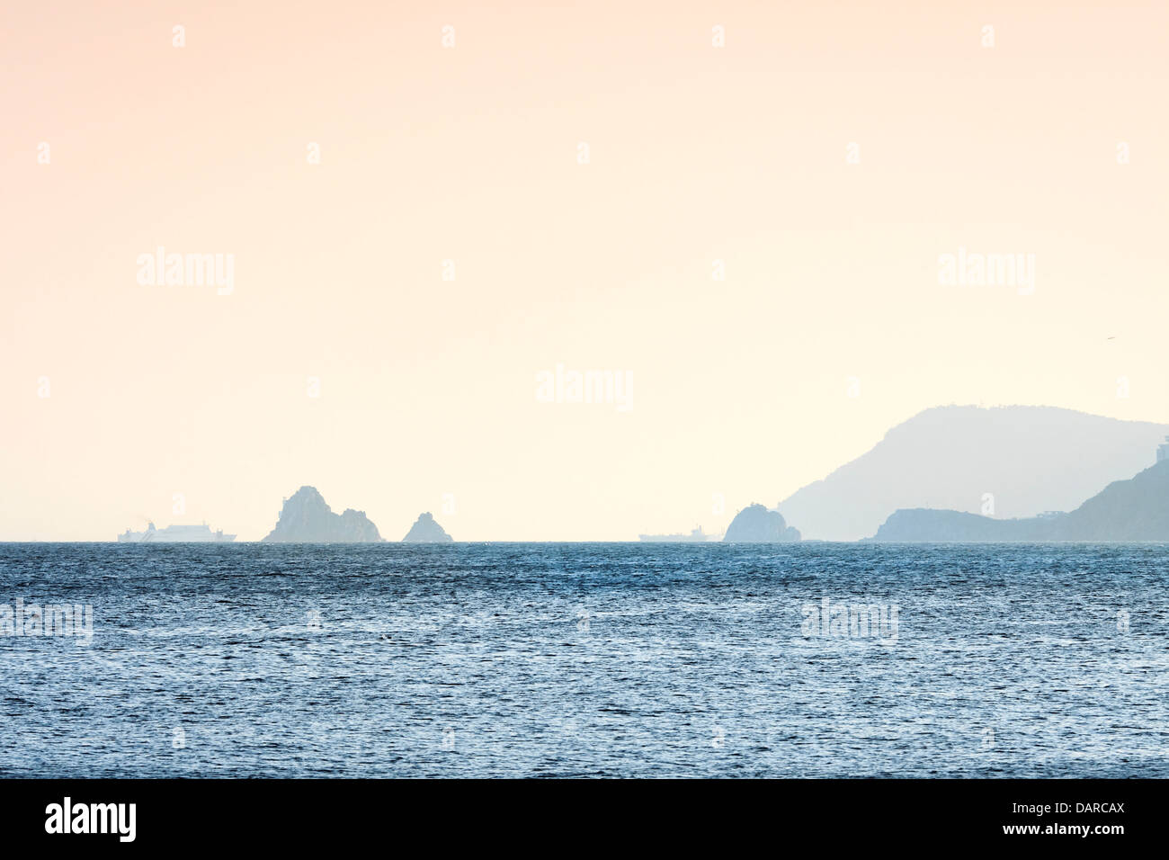 Two ships sailing in the horizon behind the Oryukdo Islands at sunset in Busan, South Korea. Seen from Haeundae Beach. Stock Photo