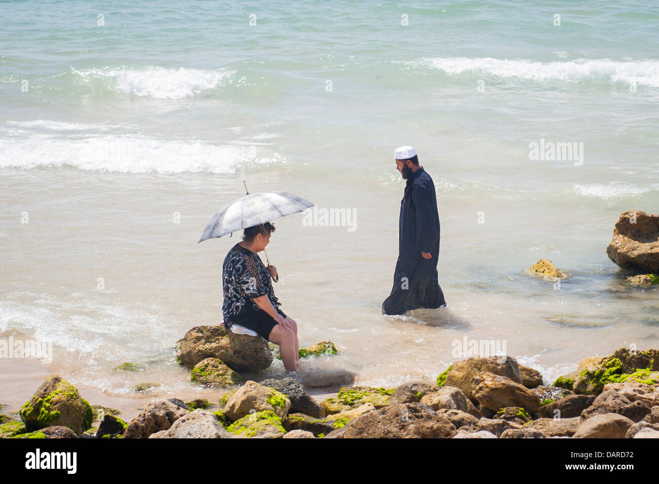 Israel Tel Aviv Jaffa Yafo Manta Ray Beach elderly lady women rock sea foam umbrella parasol sonnenschirm Arab man thorb thobe Stock Photo
