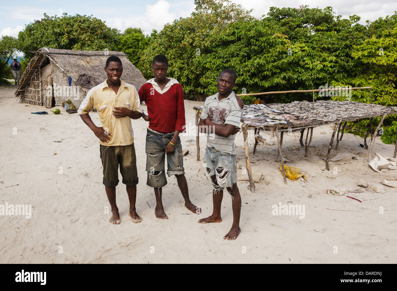 Africa, Mozambique, Ihla das Rolas. Men standing by rack of fish and traditional thatched structure. Stock Photo