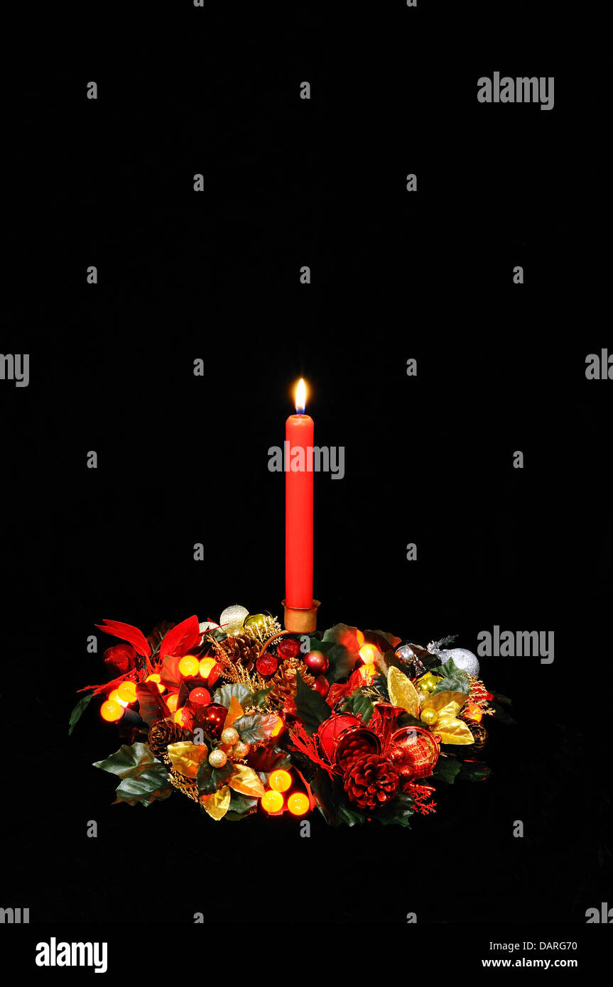 Red candle, Christmas flowers and red berry lights against a black background. Stock Photo