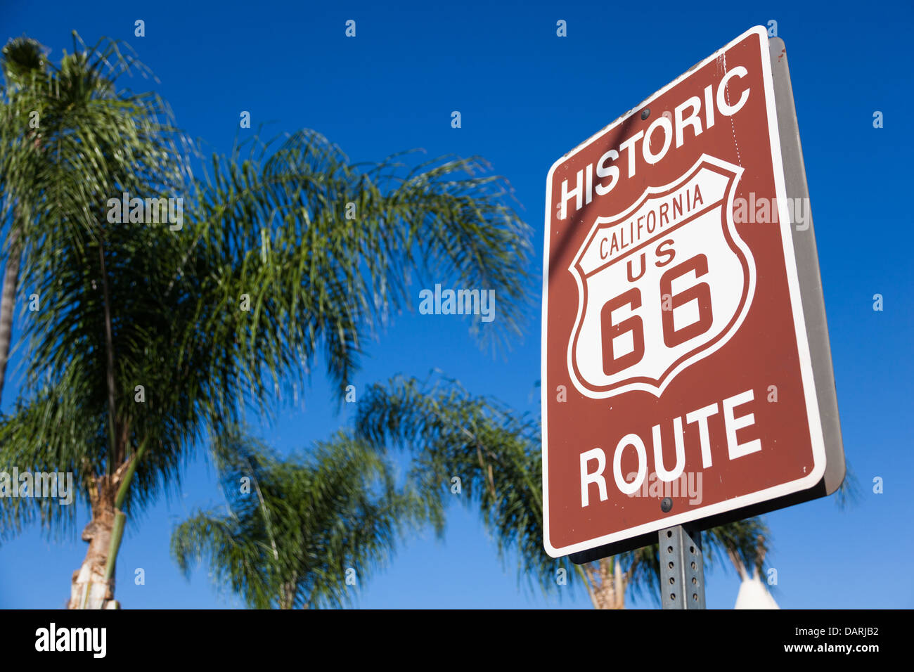 An historic route 66 highway sign with palm tree branches and a blue sky background Stock Photo